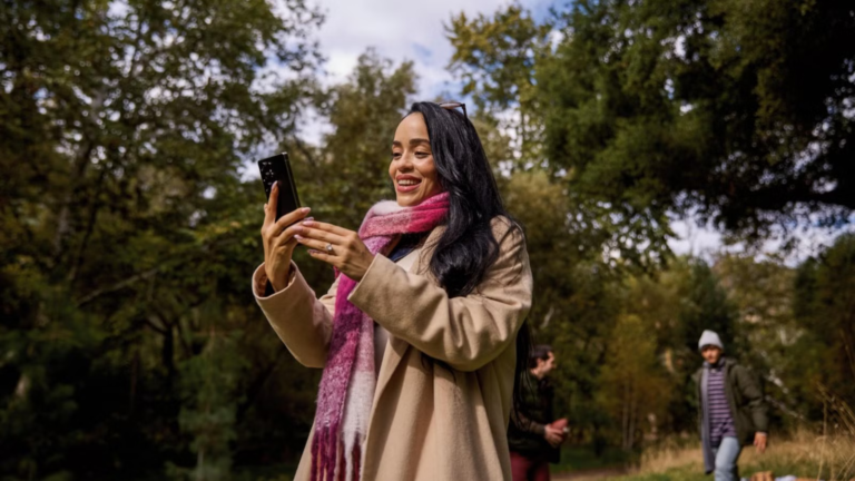 a-woman-uses-her-smartphone-in-the-park-with-her-friends-in-the-background-1920-x-1080.png